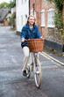 © Mint Images - Young blond woman cycling down a village street.