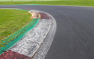 Wall Mural - Close up of rough dirty curb at left turn on motor sport track with green field and black asphalt