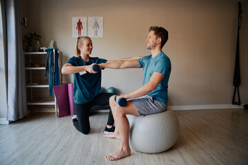 Female nurse helping young man doing stretching exercise in hospital using dumbbells