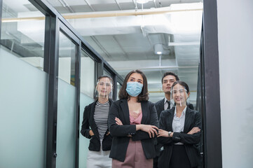 Asian business team confident wearing face mask and face shield at corridor in modern office while pandemic of virus