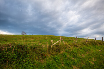 Angular view of blue sky with white clouds, hawthorn fence and green meadows in a town in Cantabria, Spain, horizontal