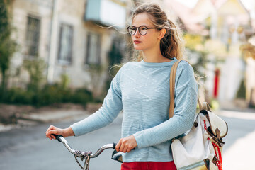 Wall Mural - Pretty student female going to the university with a bike on a sunny day outdoors. Pretty woman in casual outfit takes a rest outside after cycling.
