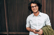 © iuricazac - Successful businessman in eyewear smiling broadly posing outdoors. Happy male entrepreneur messaging on mobile phone. Smart guy in casual wears spectacles with curly hair walking outside after work