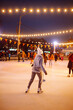 © maxbelchenko - Young woman ice skating on a rink in a Festive Christmas fair in the evening. Smiling woman in winter style clothes skates.  Winter holidays concept. Lights around.