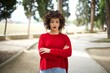 © Roquillo - Young arab woman wearing casual red sweater in the street serious face with crossed arms looking at the camera. Positive person.