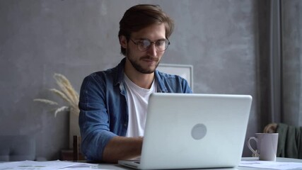 Wall Mural - Smiling businessman working on laptop computer at home office. Male professional typing on laptop keyboard at workplace. Portrait of positive business man looking at laptop screen indoors