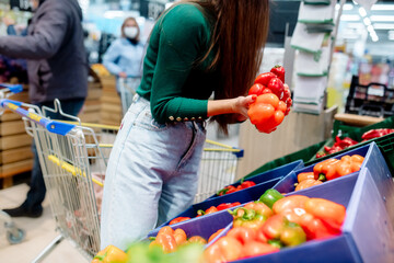 Wall Mural - Young caucasian woman chooses vegetables and fruits in a supermarket
