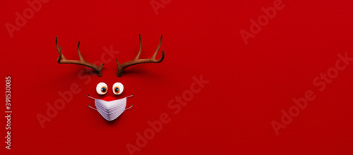 Obraz Dibond Reindeer toy with cold red nose and medical mask on red Christmas Corona background 3D Rendering