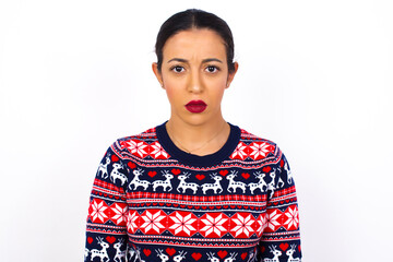 Wall Mural - Young beautiful Arab woman wearing Christmas sweater against white wall frowning his eyebrows being displeased with something.