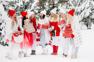 A large group of girls with Christmas gifts in their hands standing in the winter forest.Girls in red and white clothes with Christmas gifts in the snowy forest