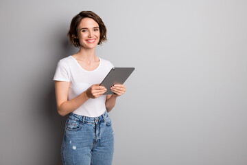 Poster - photo of cheerful positive toothy smile young woman hold computer tablet wear casual outfit isolated