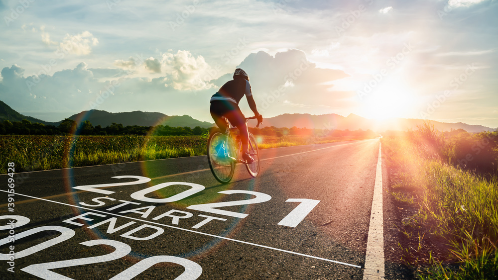 New year 2021 or start straight and beginning concept.Blurry Man ride on bike and word 2021 start written on the road at sunset add lens flare.Concept of challenge or career path,business strategy. - obrazy, fototapety, plakaty 