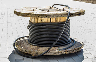 Roll of black industrial underground cable on large wooden reel at construction site. Four core al cable. Selective focus and shallow dof.