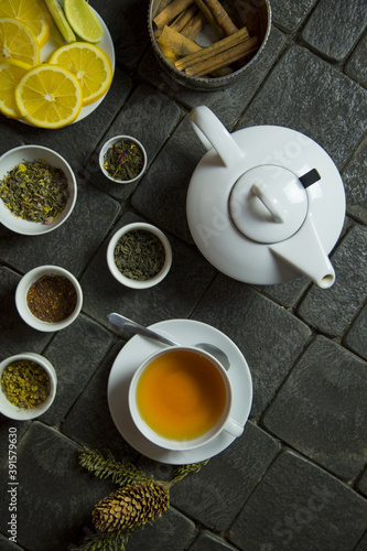 A cup of tea, a teapot, tea leaves, cinnamon and orange slices on the table