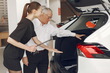 Senior in a car salon. Old man buying the car. Elegant woman helps a man buy a car.