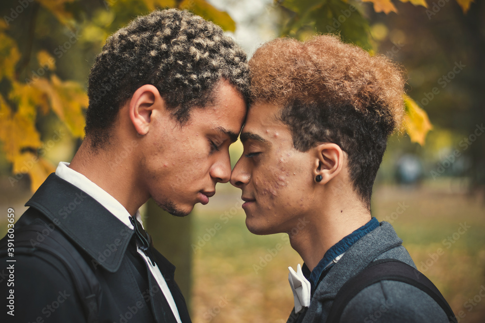 Handsome young gay couple standing head to head in park during autumn. Concept of same sex love, equality and LGBT rights. Black lives matter!