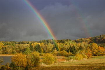  Double rainbow in countryside. Beautiful intense rainbow colors in rainy day.Weather forecast.Fall rural landscape with rainbow over dark dramatic stormy sky.Freedom happiness concept.