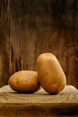 Fresh raw potatoes close-up on a board on an old wooden background. side view. artistic rustic food concept in brown tones with copy space for creative layout