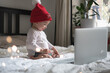 © lamapacas - Infant baby in Christmas hat chatting via lap top at home during quarantine. Social distancing during lock down. New year and Christmas celebration at home