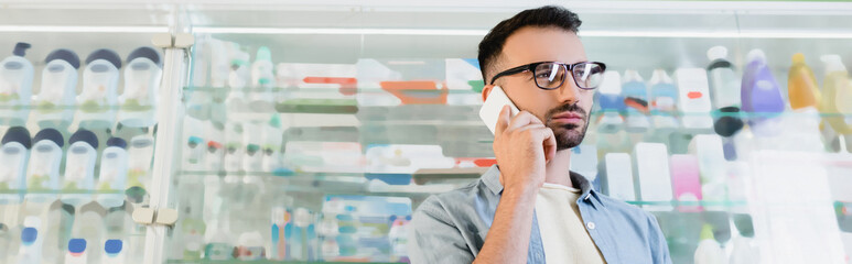 Wall Mural - man in eyeglasses talking on smartphone in drugstore, banner