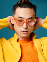 An Asian Man Wearing Orange Glasses Holds His Hands Behind His Head