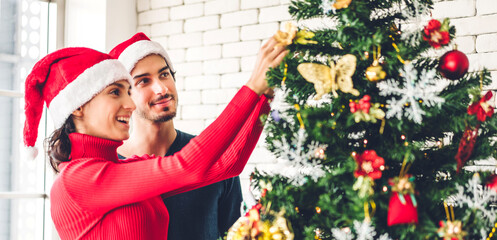 Romantic sweet couple in santa hats having fun decorating christmas tree and smiling while celebrating new year eve and enjoying spending time together in christmas time at home