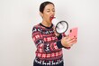 © Roquillo - Crazy impressed Young beautiful Arab woman wearing Christmas sweater against white wall,  use cell phone reads incredible news on social media information stare, screams wow omg wear stylish outfit