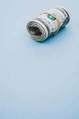 Poster - Vertical shot of a bundle of rolled-up American banknotes on a light blue background