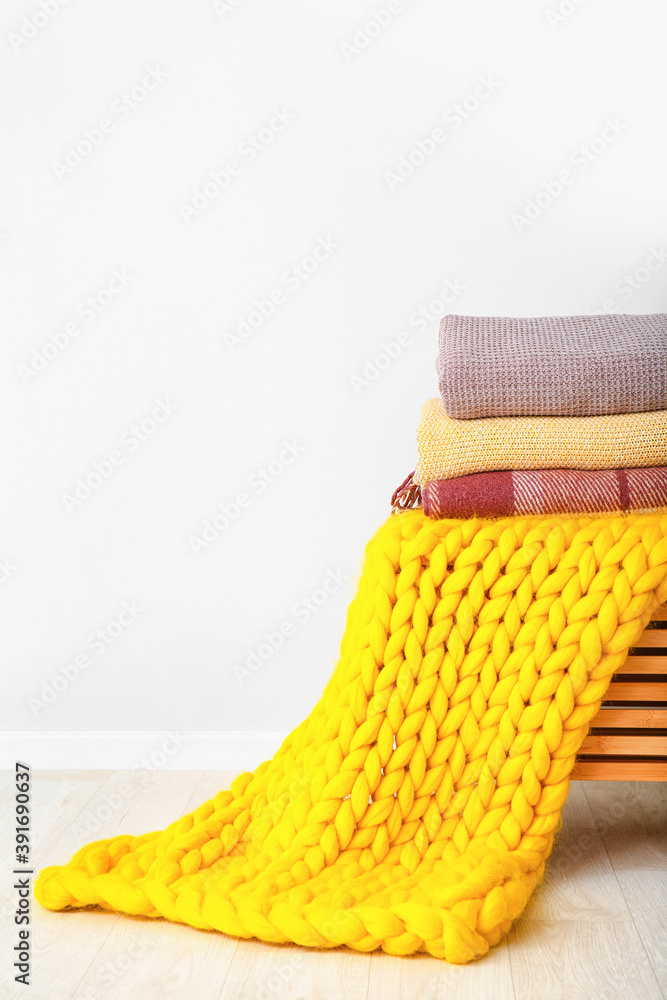 Chest with knitted plaids near light wall in room