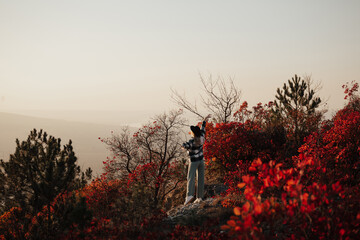 Wall Mural - Young beautiful girl with hat standing on the top of the colourful autumn hill on sunset. Soft sunny colours.  Autumn nature. Copy space.