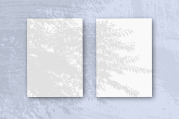 2 vertical sheets of textured white paper on soft blue table background. Mockup overlay with the plant shadows. Natural light casts shadows from an exotic plant. Horizontal orientation