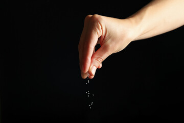 Wall Mural - Female hand adding salt on black background