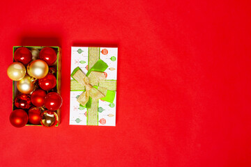 open from a green gift box with red and gold balls for the Christmas tree, next to the lid with a bow on a red background.