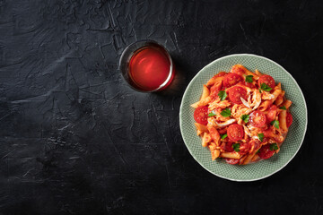 Wall Mural - Penne pasta with chicken, tomato sauce and parsley leaves, shot from above on a black background with a place for text