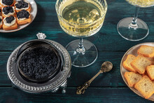 Caviar In A Vintage Bowl With A Champagne Coupe Glass, With Bread And Toasts, On A Dark Blue Wooden Background