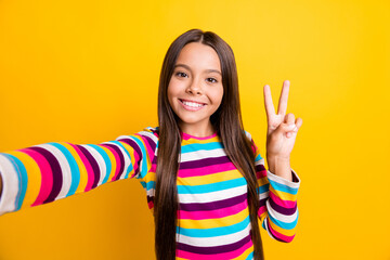 Poster - Photo of little adorable girl take selfie show v-sign beaming smile wear striped shirt isolated yellow color background