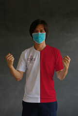 Wall Mural - Man wearing hygienic mask and wearing Malta flag colored shirt and standing with raised both fist on dark wall background.