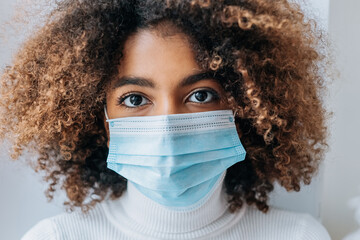 Wall Mural - Pretty model with big brown eyes and short hairstyle wearing protective facial mask against white background extreme close view