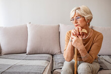 Shot Of A Senior Woman Holding Onto Her Walking Stick While In The Living Room Of A Nursing Home. Wrinkled Hands Holding Walking Stick. Shot Of A Senior Woman Leaning On Her Wooden Walking Stick