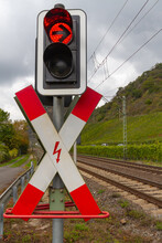 Red And White Traffic Sign For Railroad Crossing With A Red Stoplight In Front Of A Green Landscape And A Gray Sky