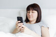 © Di Studio - woman using smart phone lying in bed at home