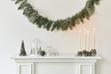 Christmas composition on the white chimney at the living room interior with beautiful decoration. Christmas tree and wreath, candles, stars, light. Copy space. Template.