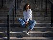 © Adamov - Tranquility. Full length of beautiful young mixed race woman in casual wear looking aside while sitting on stairs outdoors on a warm sunny day. Selective focus. Medium format shot
