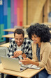 © Friends Stock - Two young happy diverse colleagues looking at laptop and discussing something while sitting at the desk in coworking space