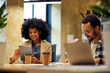 © Friends Stock - Two young happy multiracial business people sitting at the desk, using modern technologies while working together in coworking space