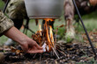 Hand of Man Sets Fire under Cooking Pot in Forest.
