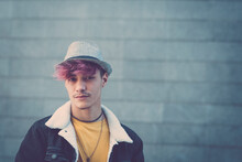 Portrait Of Handsome Alternative Trendy Young Man Teenager Boy With Violet Hair And Hat - Youth People With Piercing And Coloured Hair Looking On Camera With Grey Wall In Background