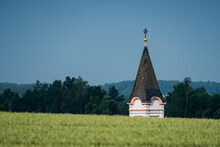 Typical Lower Bavarian Church Bell Tower Hidden Behind Hill With Field Of Growing Wheat Against Blue Sky