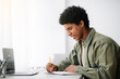 © Prostock-studio - Web-based training concept. Black male student writing in notebook in front of laptop at home, empty space