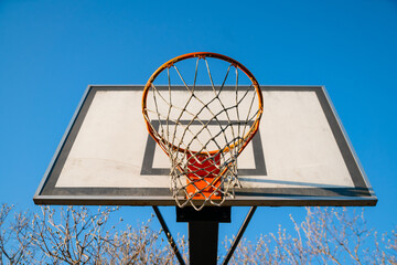 Wall Mural - Street basketball hoop on a sunny day with blue sky in the background. Urban youth game. Concept of success, scoring points and winning